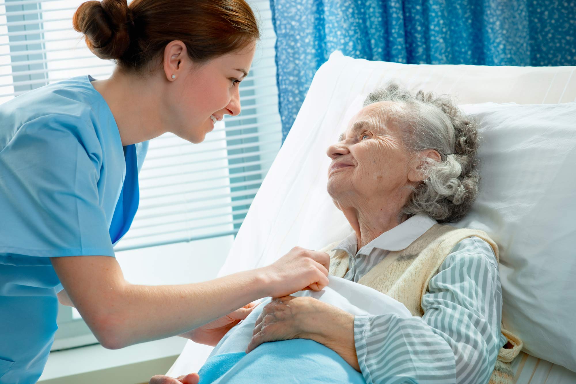 Krankenschwester kümmert sich um eine ältere Frau, die im Bett liegt: © Alexander Raths – stock.adobe.com